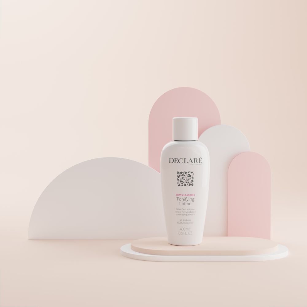 Witte fles met dop op een sokkel. Opschrift: DECLARÉ, logo, Toning Lotion. Achtergrond: beige, roze en wit.