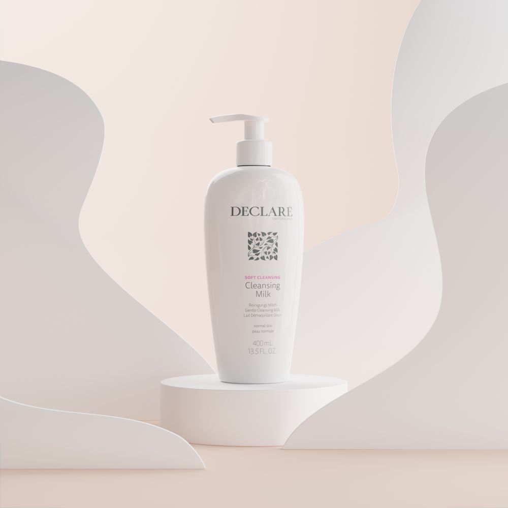 Witte fles met pomp op sokkel. DECLARÉ Cleansing Milk, 400ml. Achtergrond met witte vormen.
