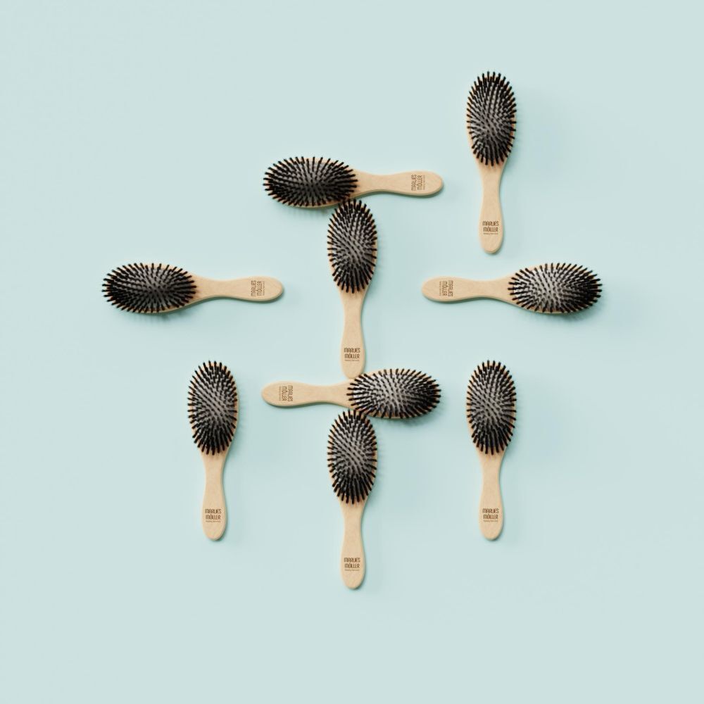 Meerdere kleine ovale haarborstels op turquoise achtergrond. Houten handvat, zwarte borstelharen.