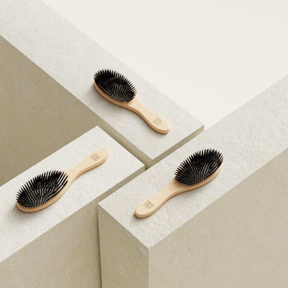 Trois brosses à cheveux sur blocs blancs. Tête ovale, manche en bois, soies noires.