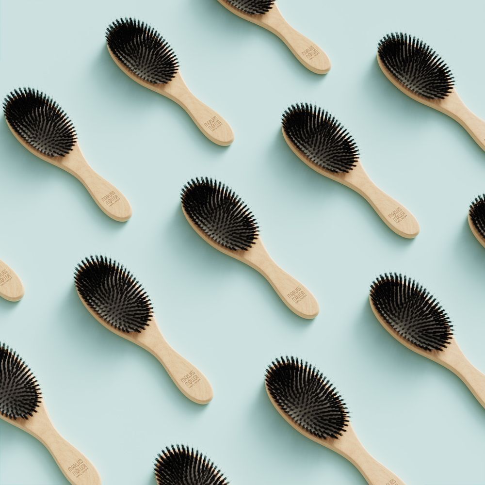 Plusieurs brosses à cheveux ovales, manche en bois, soies noires, sur fond bleu clair.