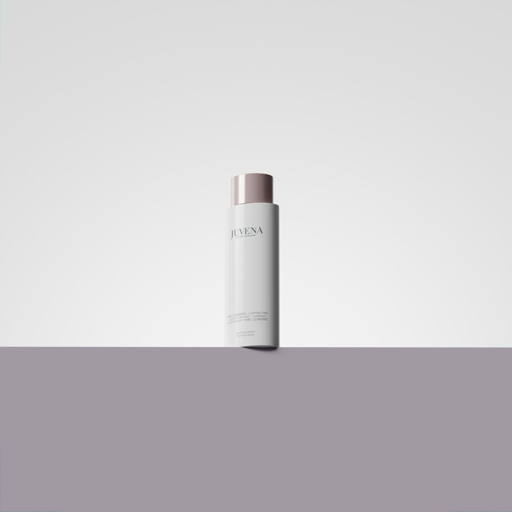 Flacon blanc avec bouchon rose. Inscription : Juvena. Le produit est posé sur une ligne violette.