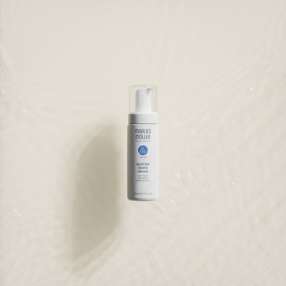 Witte fles met spuitkop. Opschrift: Marlies Möller, beauty haircare, Volume, Liquid Hair Keratin Mousse. Op lichte achtergrond.