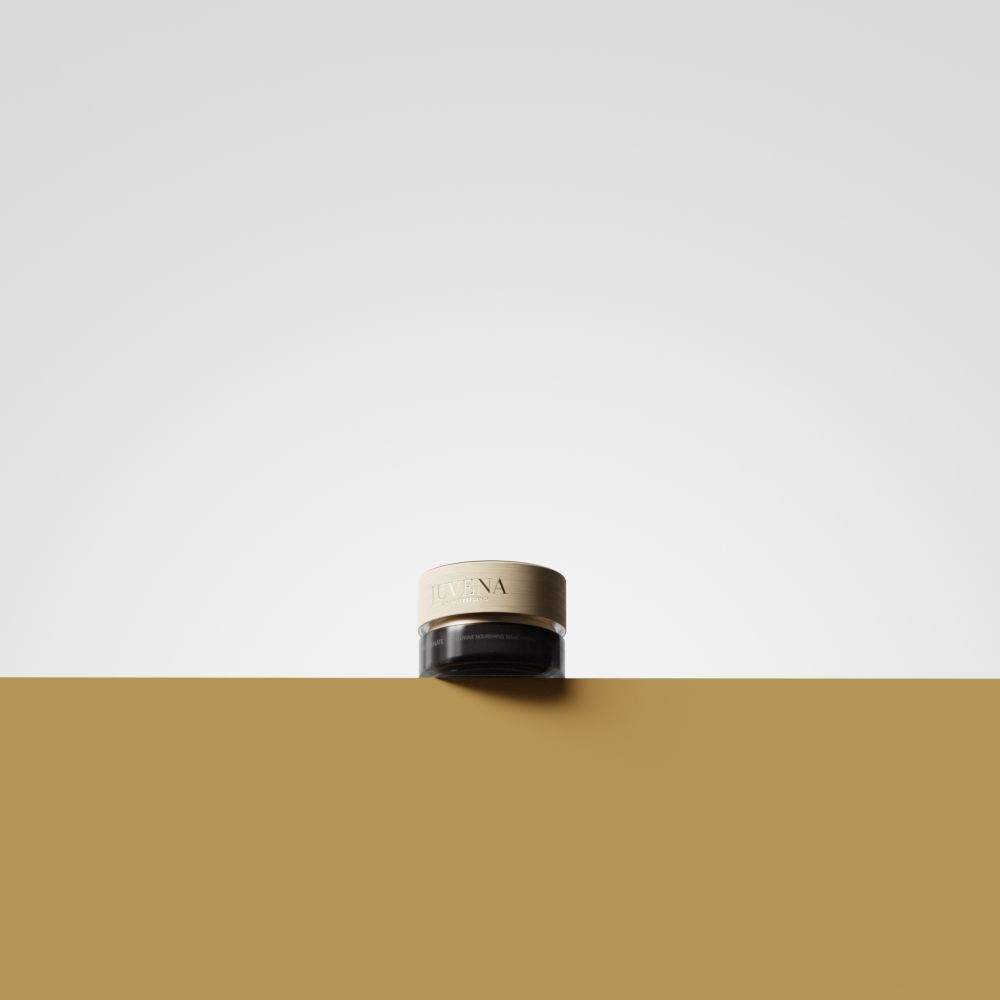 Pot de crème avec couvercle doré. Inscription : JUVENA. Placé sur une surface dorée. Fond : jaune et blanc.