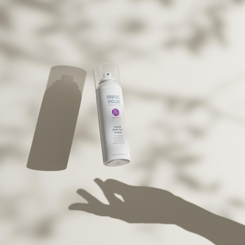 Wit haarspray van Marlies Möller. Schaduw van een hand. Opschrift: Crystal Shine Hair Lacquer.
