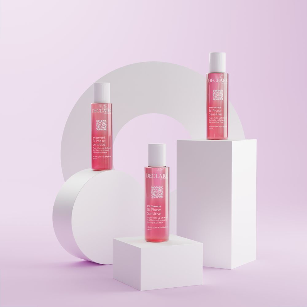 Trois flacons. Liquide rose, bouchons blancs. Texte: DECLARE, EYE CONTOUR, Bi-Phase Sensitive. Sur blocs blancs.