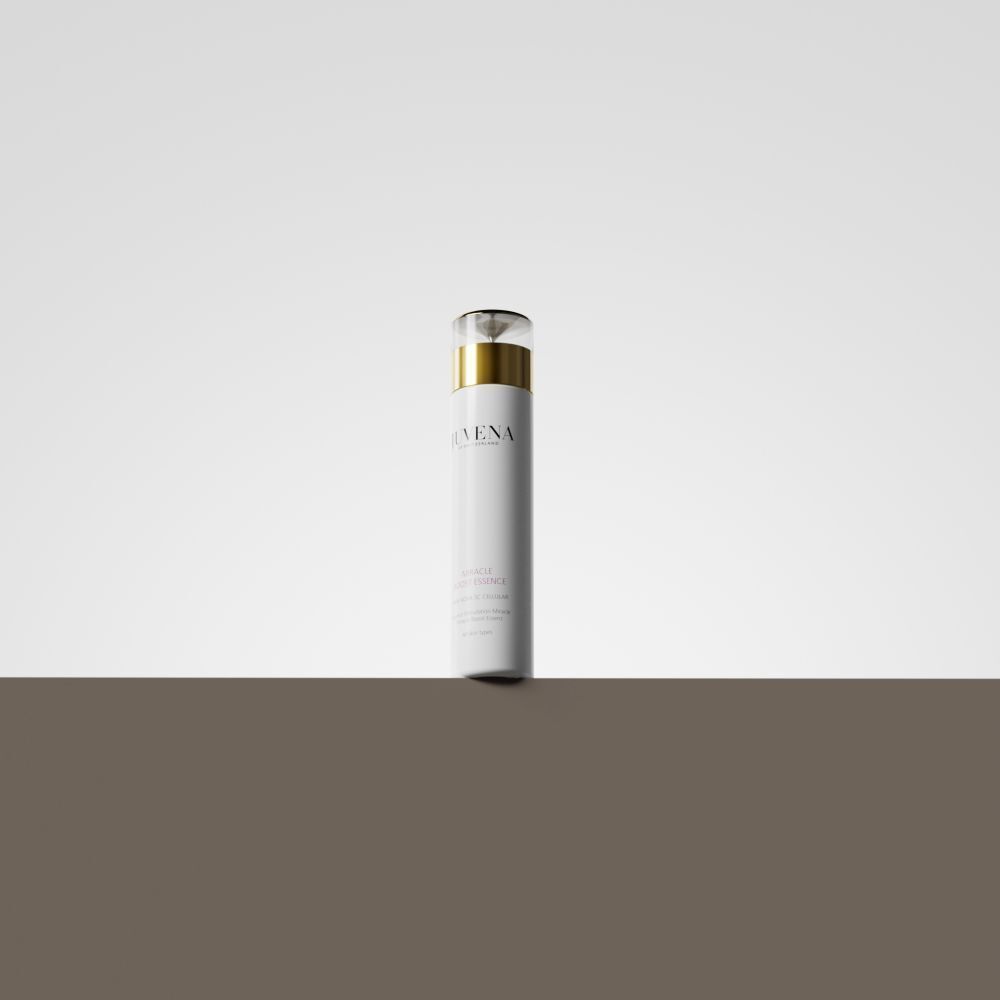 Flacon blanc avec bouchon doré. Inscription: Juvena, Miracle Boost Essence. Sur fond marron.