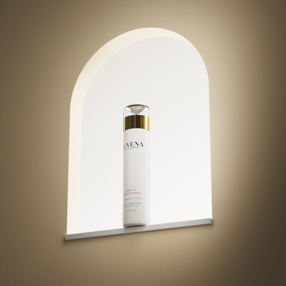 Flacon blanc avec bouchon doré. Inscription: Juvena, Miracle Boost Essence. Dans une niche blanche.