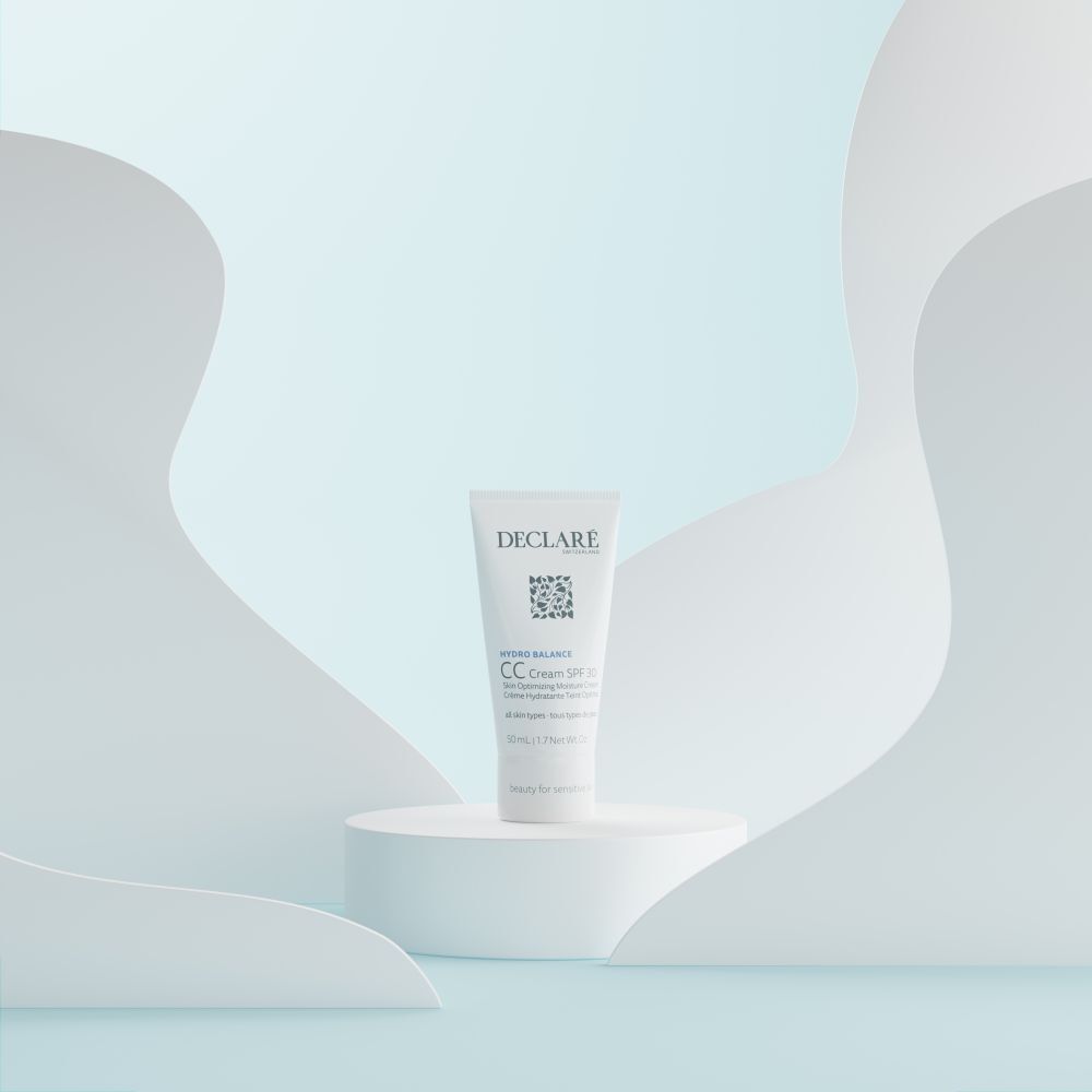 Witte tube DECLARÉ CC Cream SPF 30 op een sokkel. Achtergrond met witte, golvende vormen.