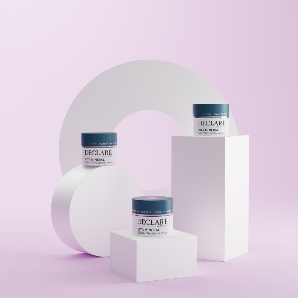 Drie crèmepotten op voetstukken. DECLARÉ Vita Mineral Q10 Multi-Vitamin Crème. Roze achtergrond.
