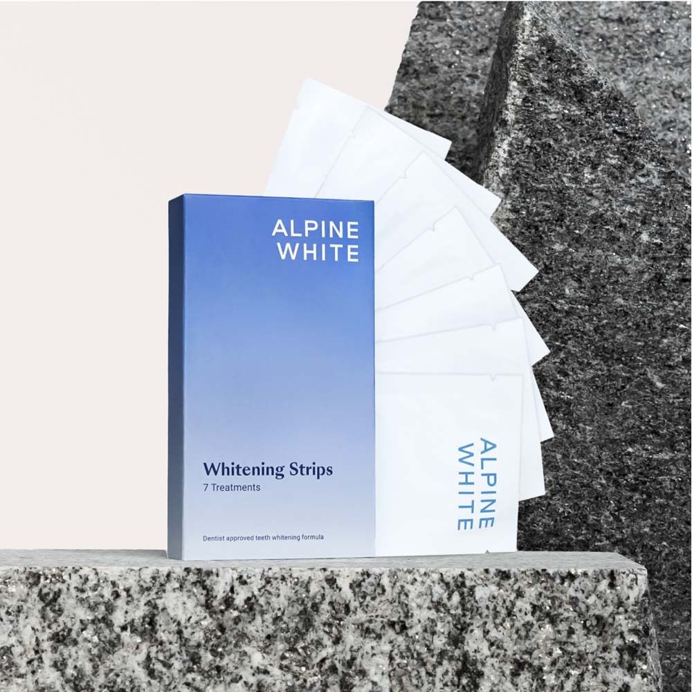 Boîte bleue et blanche ALPINE WHITE Whitening Stripes. 7 traitements. Posée sur une pierre.