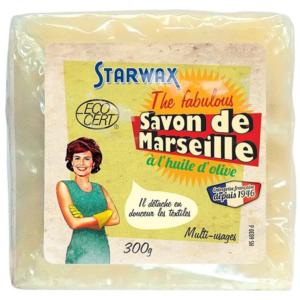 Vierkant blok zeep in folie. Etiket met productnaam, merk STARWAX en ECO CERT-logo. Vrouw met gele handschoenen.