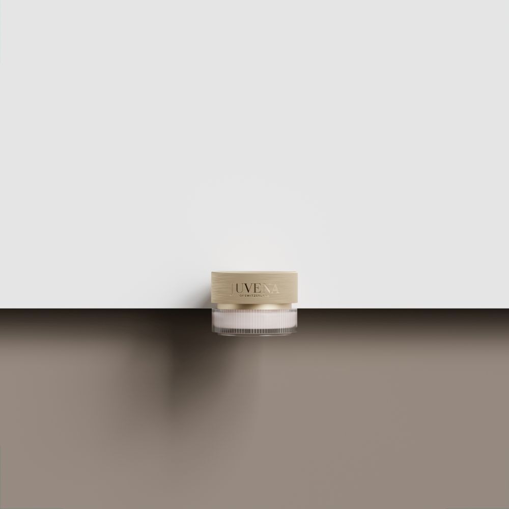 Un pot de crème avec un couvercle doré est posé sur une surface marron. Le fond est blanc.