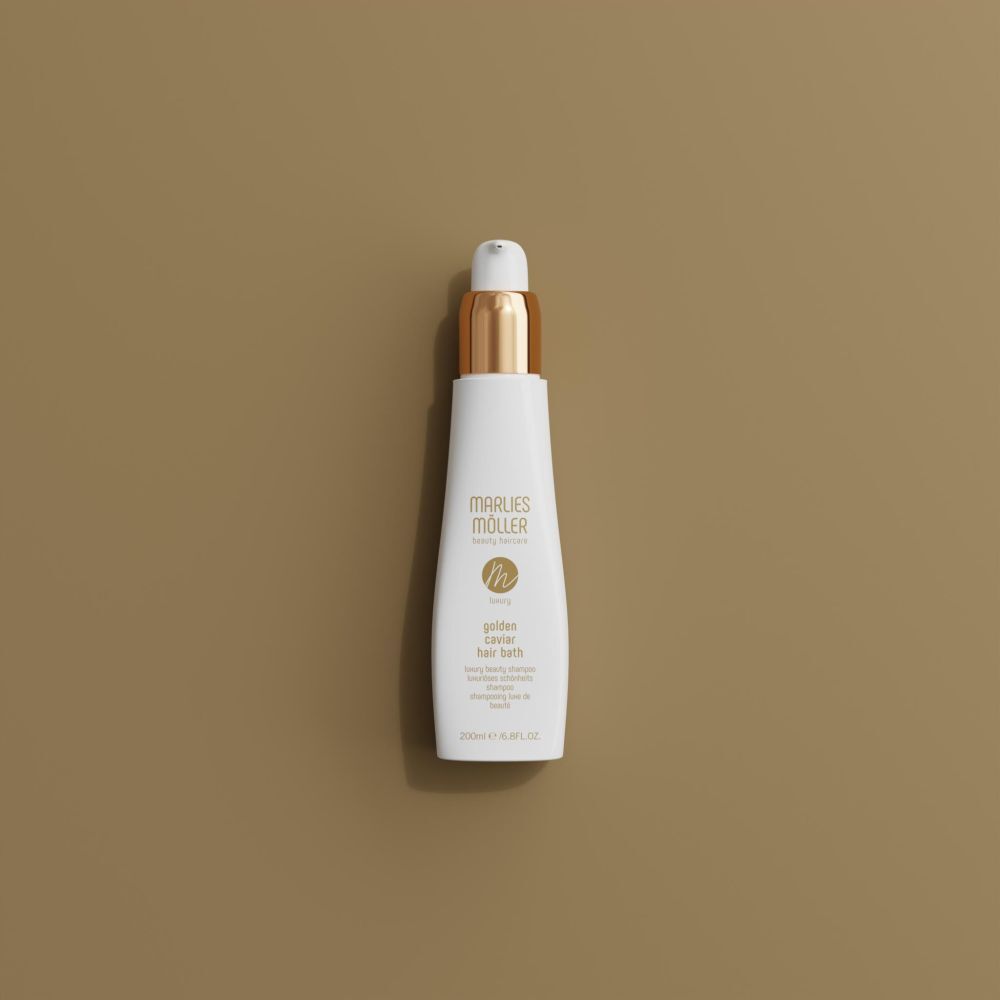 Flacon blanc avec bouchon doré. Inscription: Marlies Möller, Luxury Golden Caviar Hair Bath. Sur fond marron.
