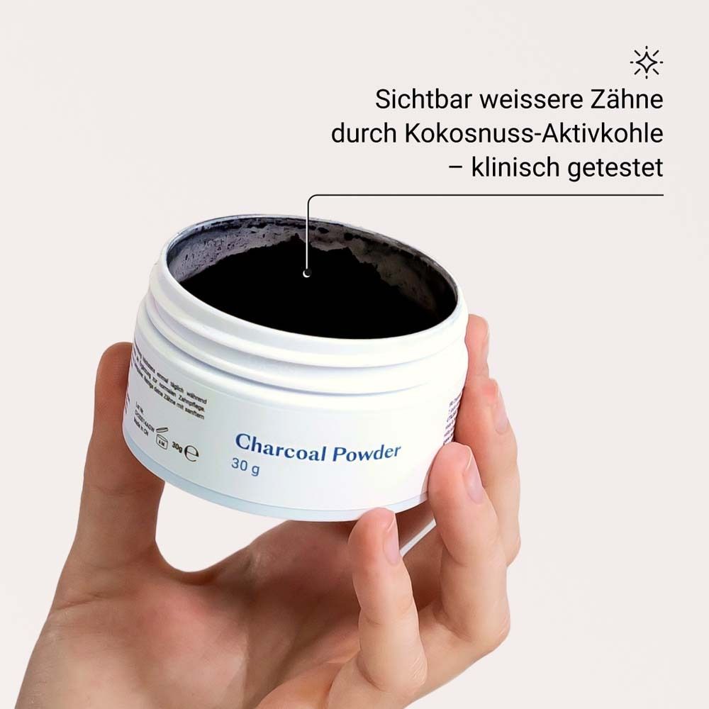 Main tenant un pot de "Charcoal Powder". Poudre noire visible. Texte: Dents plus blanches grâce au charbon actif de noix de coco.