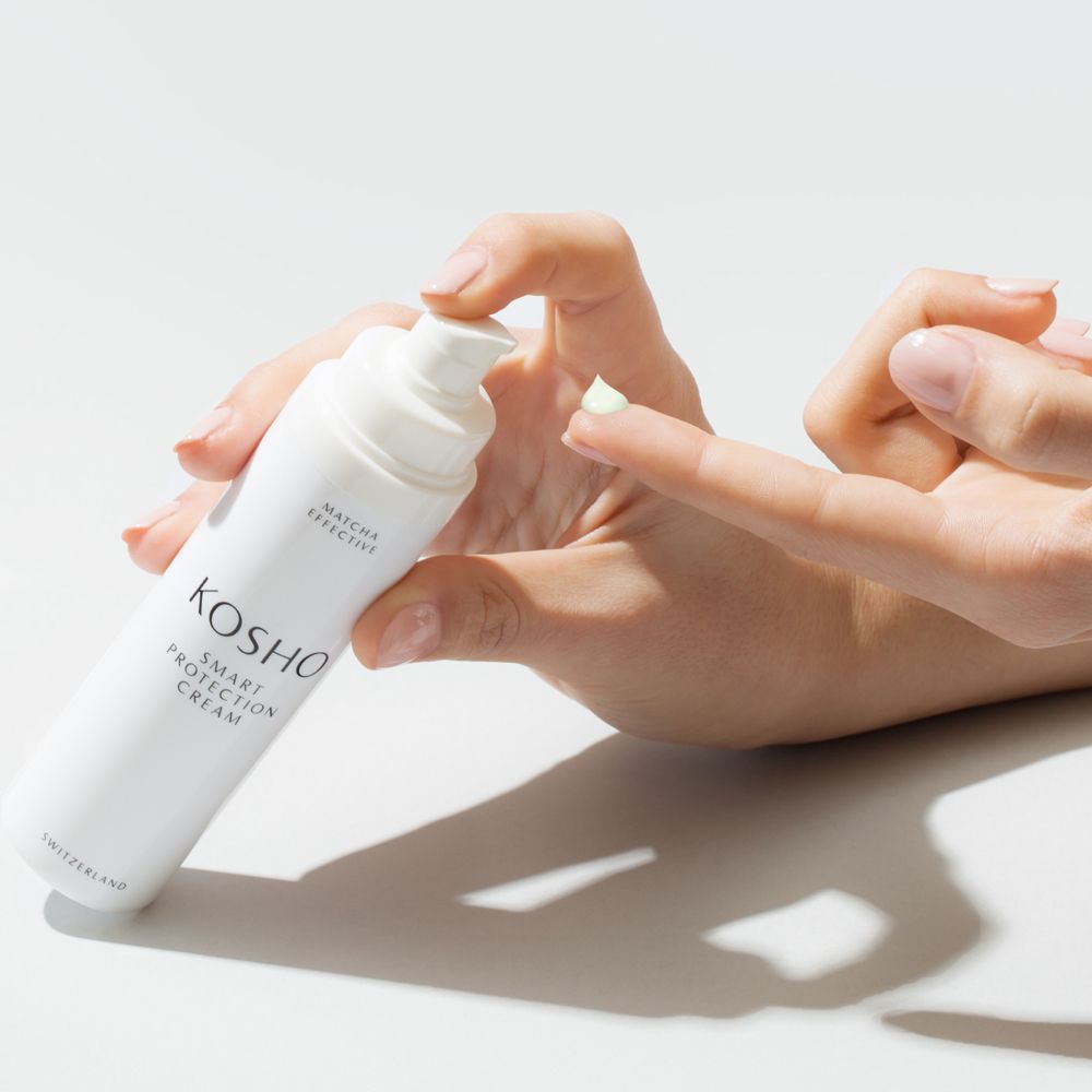 Persoon houdt tube vast en drukt crème op vinger. Witte tube met opschrift: KOSHO SMART PROTECTION CREAM.
