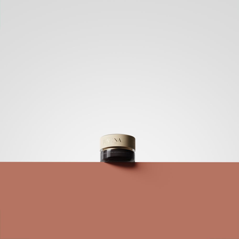 Crèmepot met gouden deksel op rode ondergrond. Alleen deksel zichtbaar. Opschrift: Juvena.