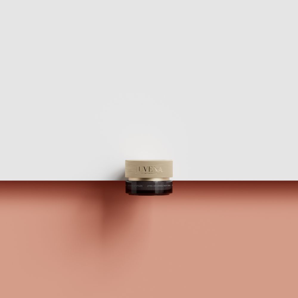 Crèmepot met gouden deksel op rode ondergrond. Alleen deksel zichtbaar. Opschrift: Juvena.