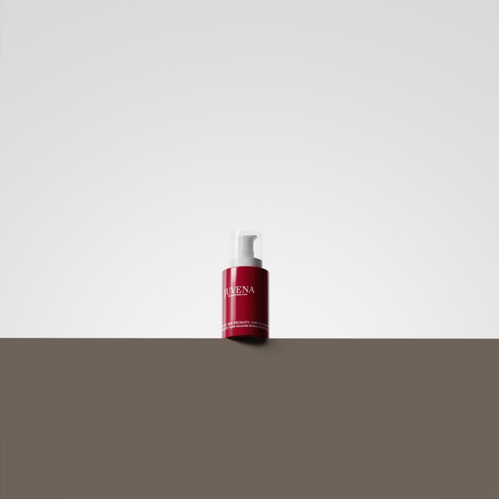 Flacon rouge avec pompe blanche. Inscription: JUVENA. Le produit est sur un fond marron devant un fond blanc.