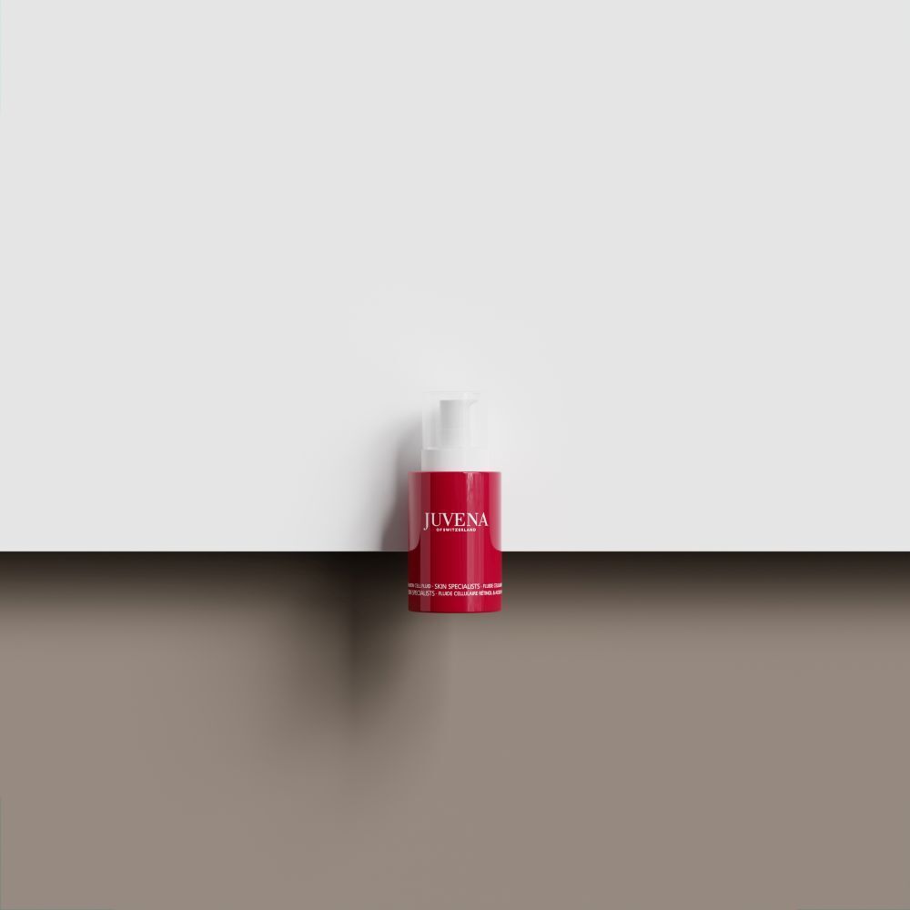 Flacon rouge avec pompe blanche. Inscription: JUVENA. Le produit est sur un fond marron devant un fond blanc.