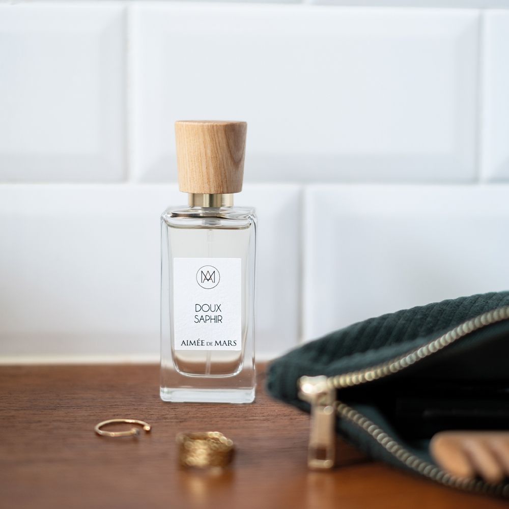 Flacon de parfum avec bouchon en bois, près de bijoux et d'une trousse. Étiquette: "Doux Saphir".