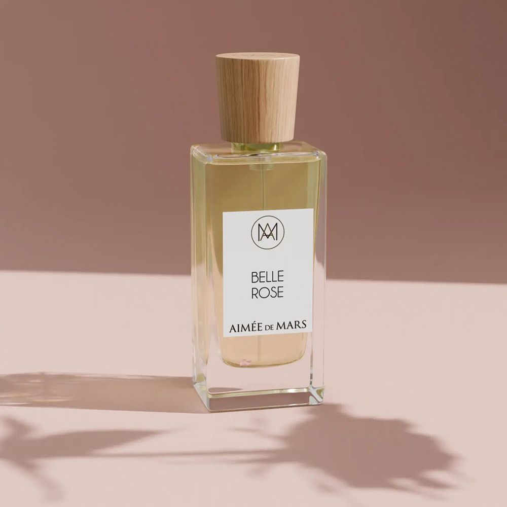 Flacon de parfum avec bouchon en bois. Étiquette : Belle Rose, Aimée de Mars. Fond rose.