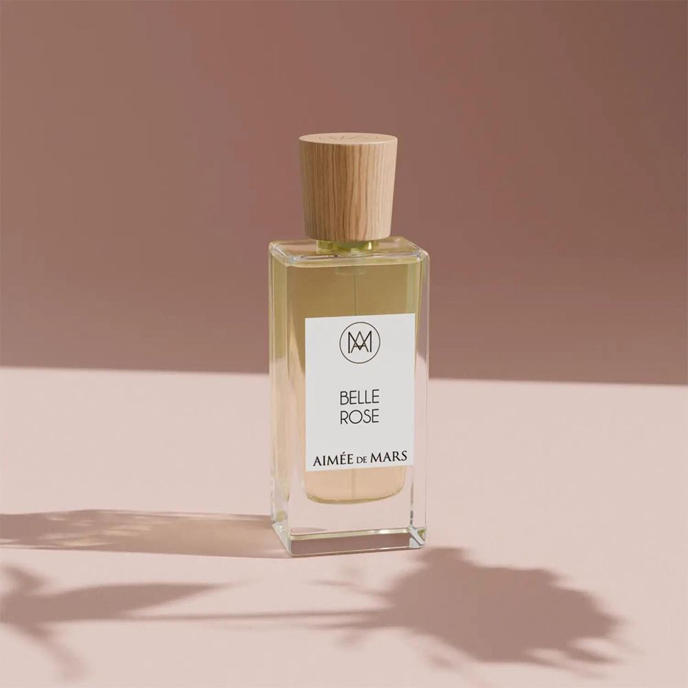 Flacon Aimée de Mars Belle Rose Eau de Parfum. Bouteille rectangulaire en verre, bouchon en bois. Sur fond rose avec ombre.