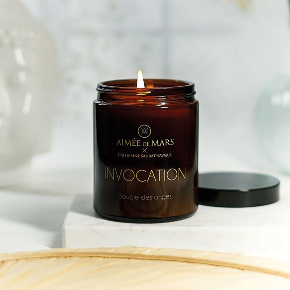 Bougie parfumée marron allumée avec couvercle noir. Inscription dorée: Aimée de Mars, Invocation, Bougie des anges.