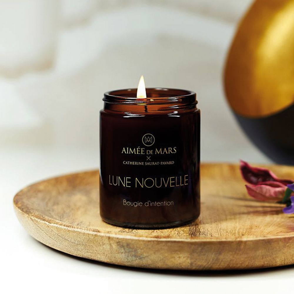 Bougie brune allumée en pot de verre avec couvercle noir. Inscription : Aimée de Mars, Lune Nouvelle, Bougie d'intention.