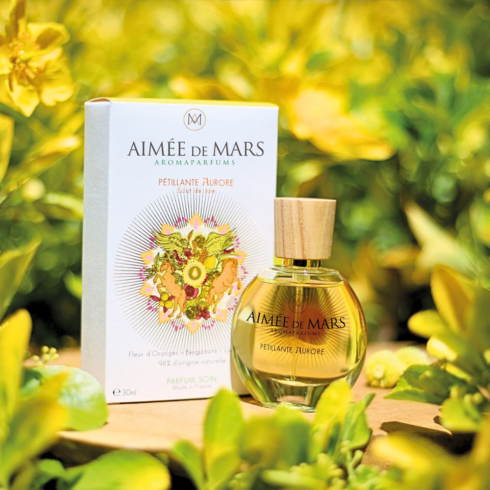 Flacon de parfum et boîte devant un fond vert. Boîte avec inscription : Aimée de Mars, Pétillante Aurore.