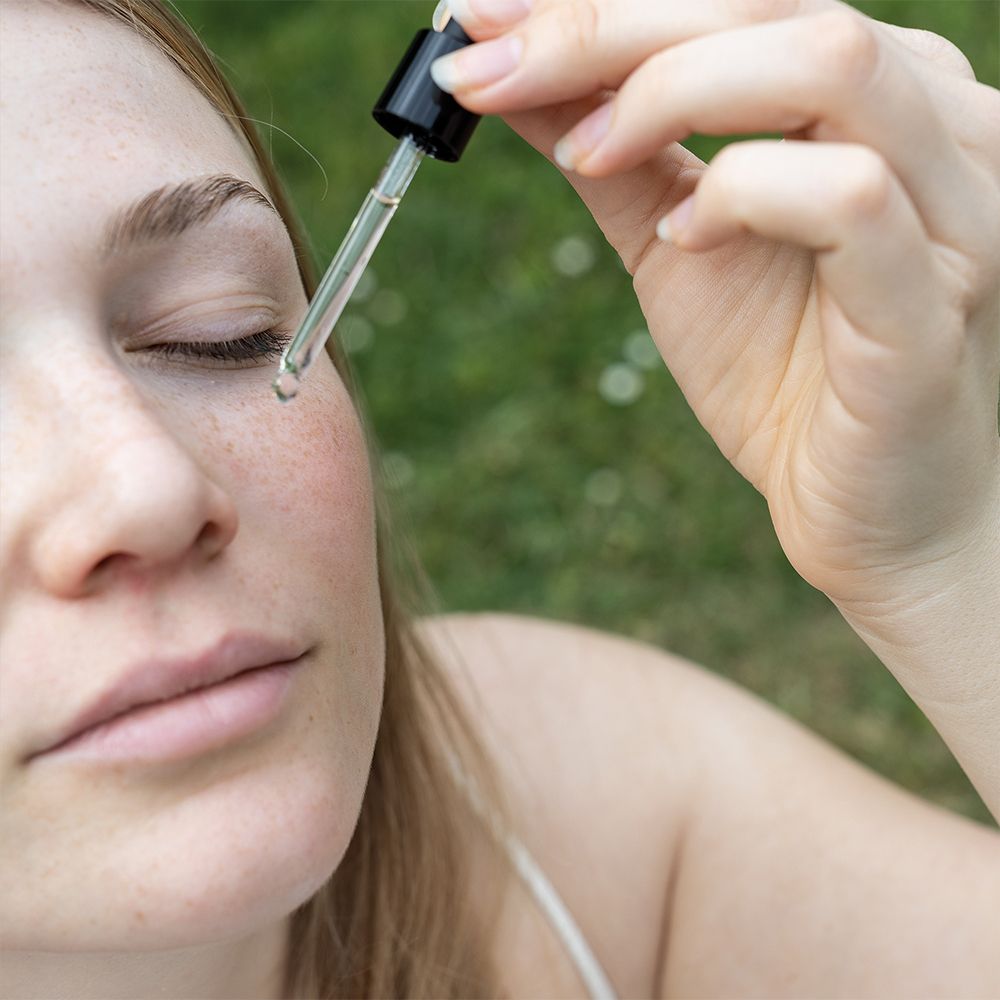 Vrouw met gesloten ogen. Druppelaar brengt vloeistof op de huid aan. Groene achtergrond.