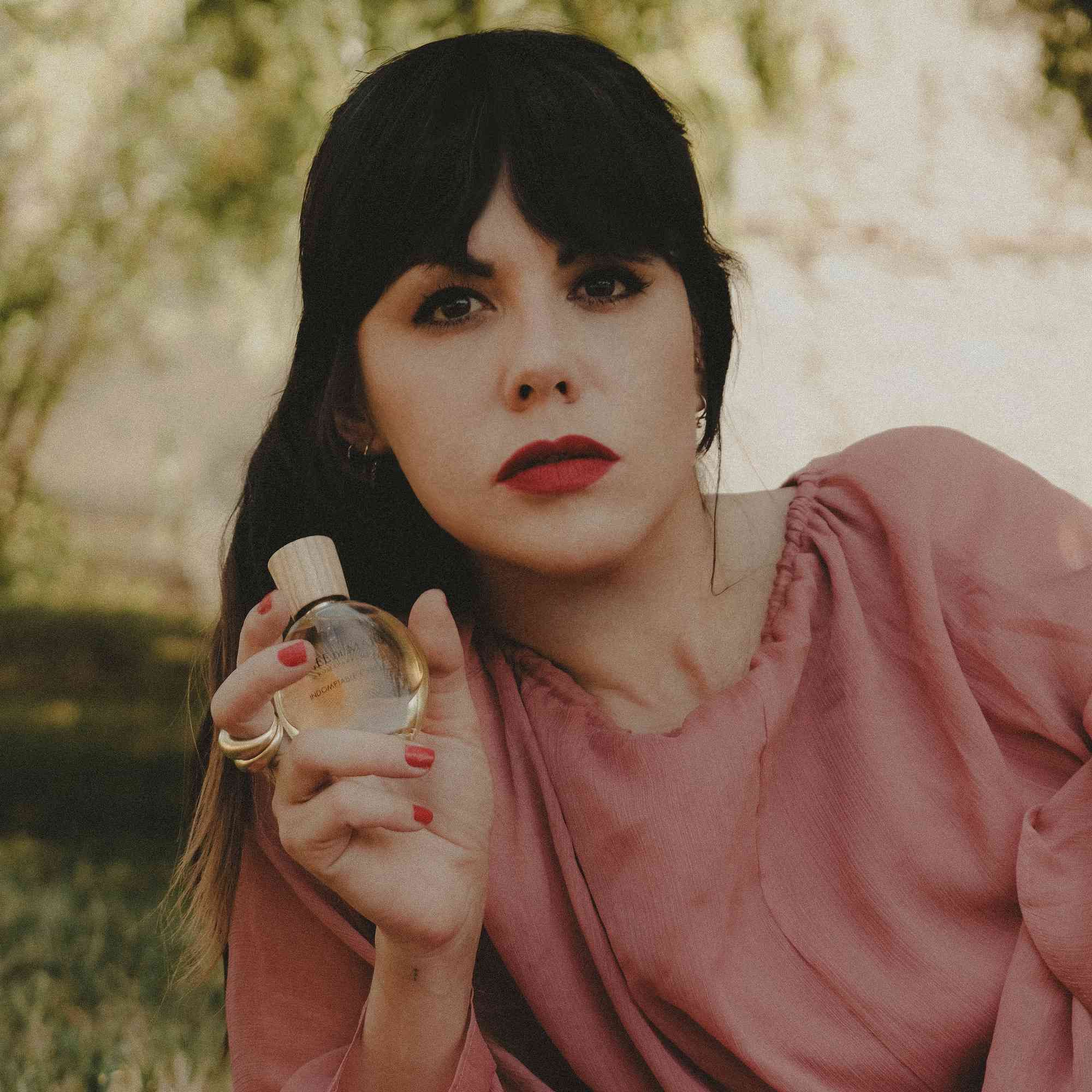 Vrouw houdt een flesje vast. Ze draagt rode lippenstift en een ring. Het flesje is zichtbaar.