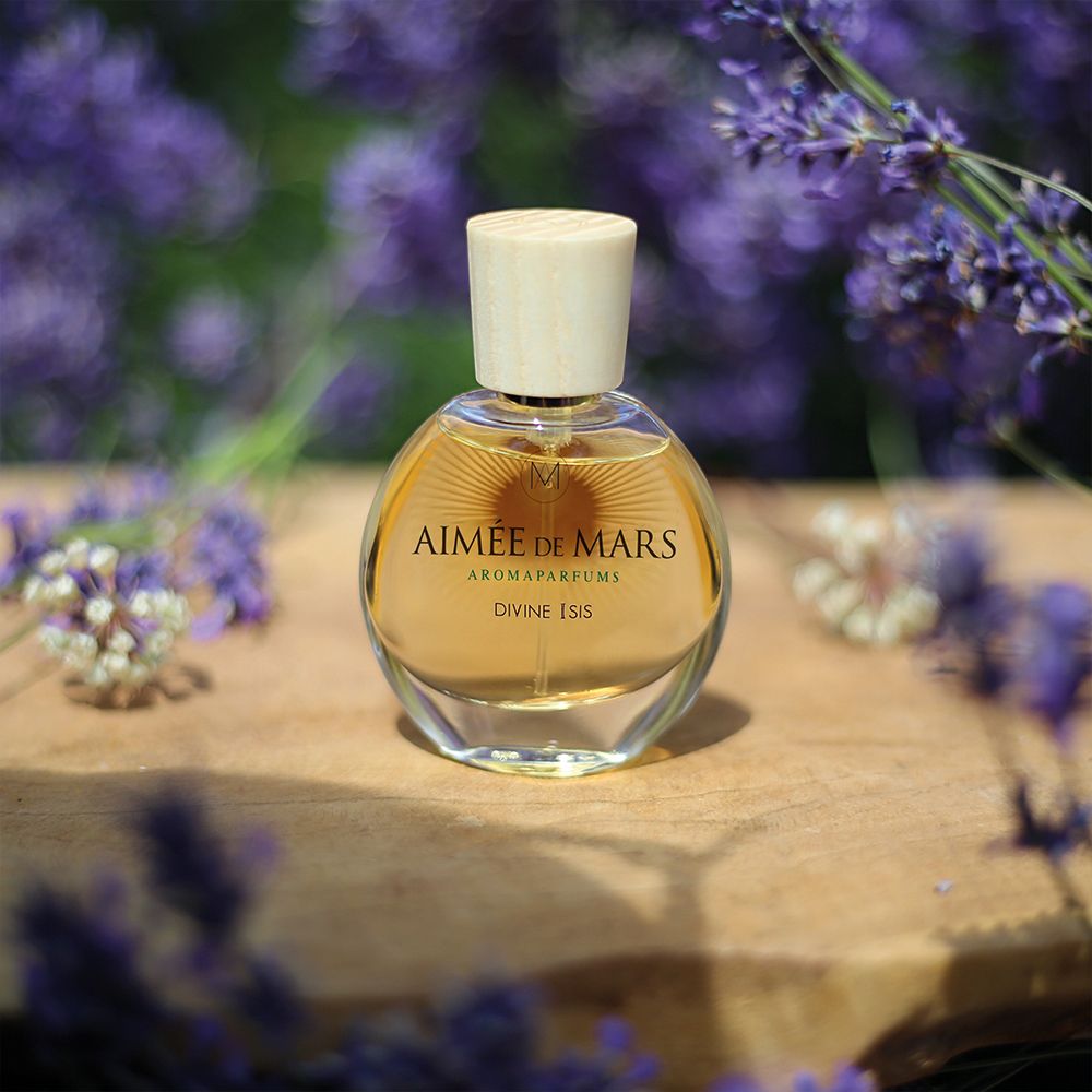 Fles op hout. Fles: rond, glas, houten dop. Opschrift: Aimée de Mars, Divine Isis. Omringd door lavendelbloemen.
