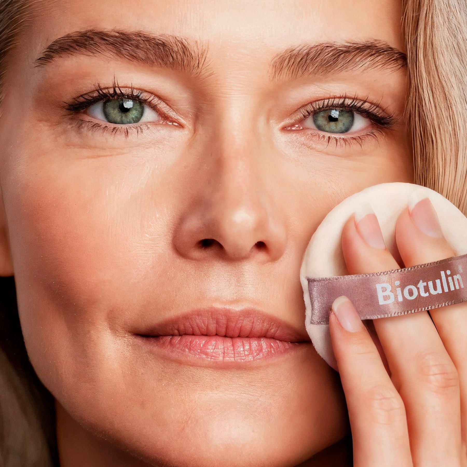 Femme avec houppette. Biotulin est visible sur la houppette. Fond clair.
