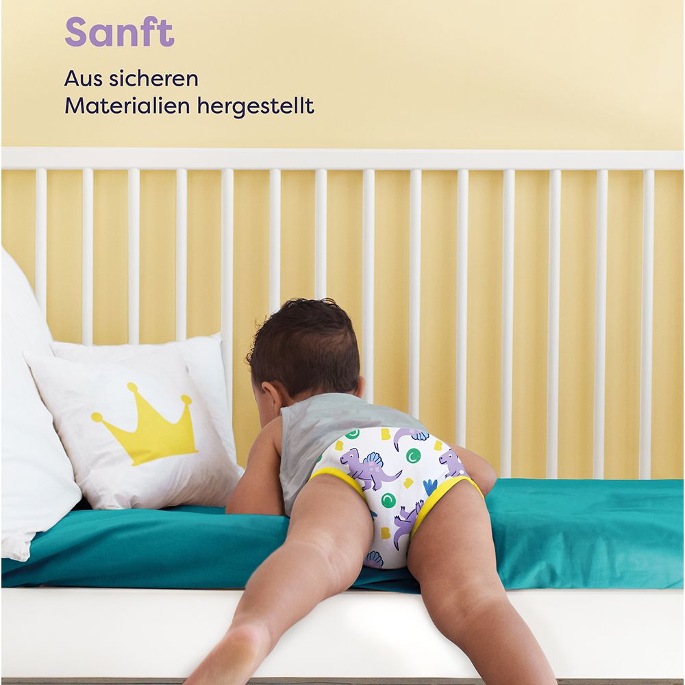 Kind met oefenbroekje op bed. Tekst: Zacht. Gemaakt van veilige materialen. Geel kussen met kroon.
