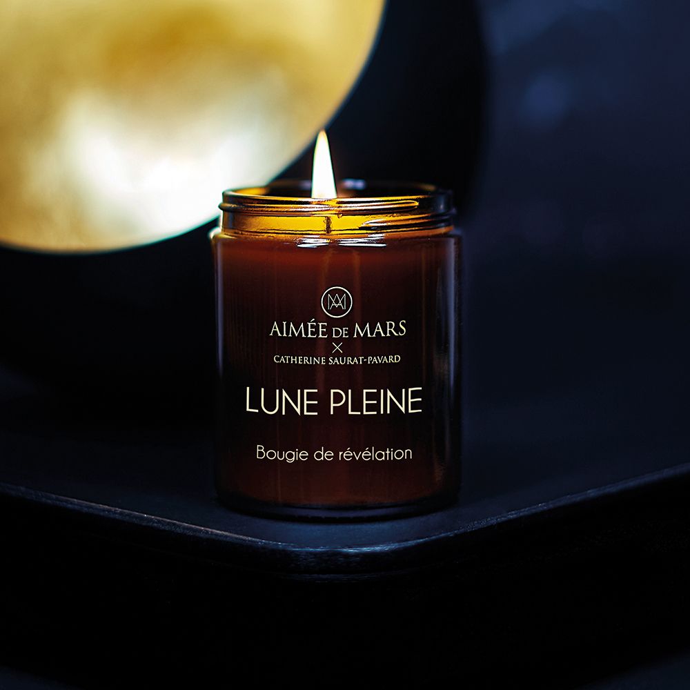 Bougie brune allumée en pot de verre avec couvercle noir. Inscription: AIMÉE DE MARS, LUNE PLEINE, Bougie de révélation.