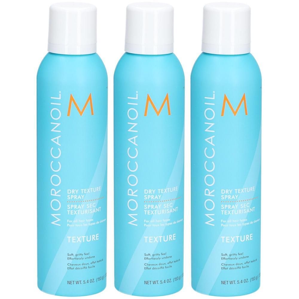 Trois flacons de spray texturisant sec Moroccanoil bleus avec bouchons blancs. Logo et nom du produit visibles.