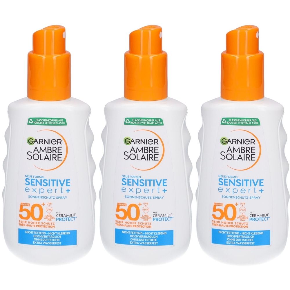 Trois flacons de spray solaire avec bouchon orange. Inscription: GARNIER AMBRE SOLAIRE Sensitive Expert+ 50.