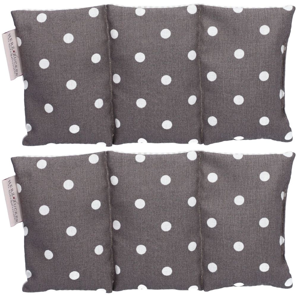 Deux coussins chauffants à pois blancs sur tissu gris. L'étiquette indique "HERZZUCKER".