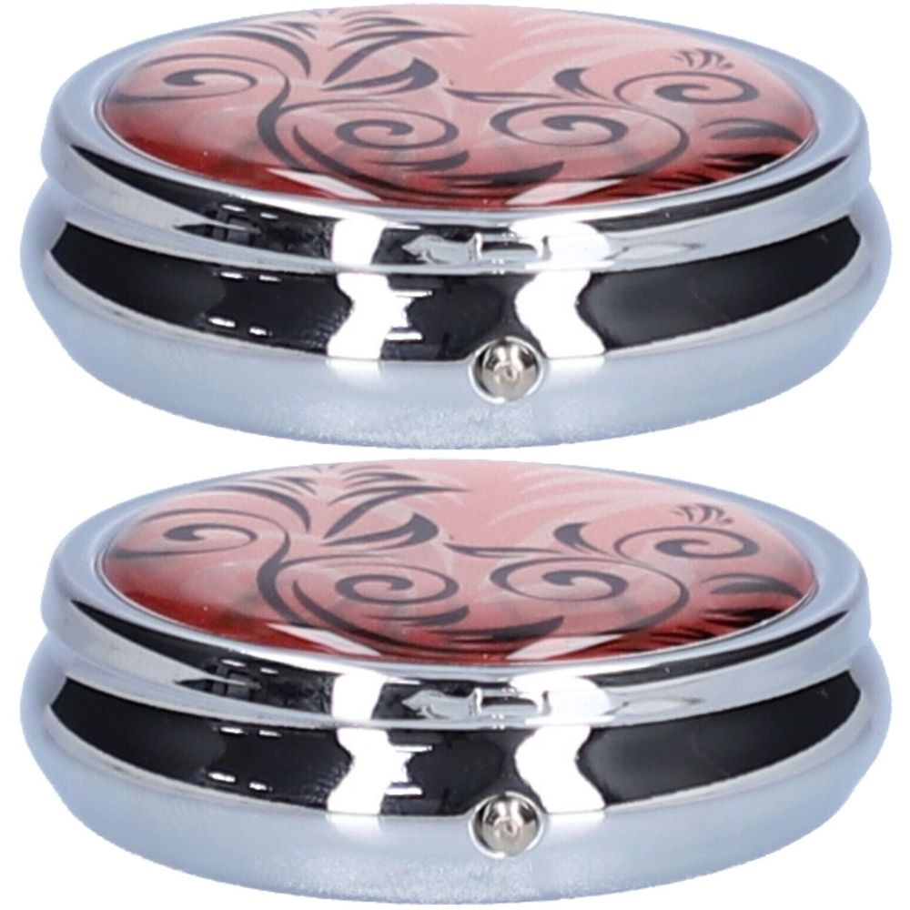 Deux piluliers ronds avec boîtier argenté et couvercle rose orné d'un motif floral noir. Chaque pilulier est doté d'une fermeture.