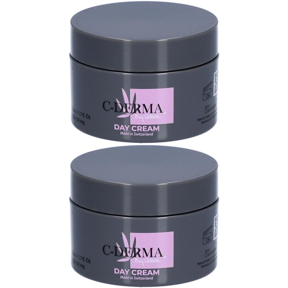 Twee potten C-DERMA Day Cream. Grijze deksels, roze etiket met tekst. Made in Switzerland.