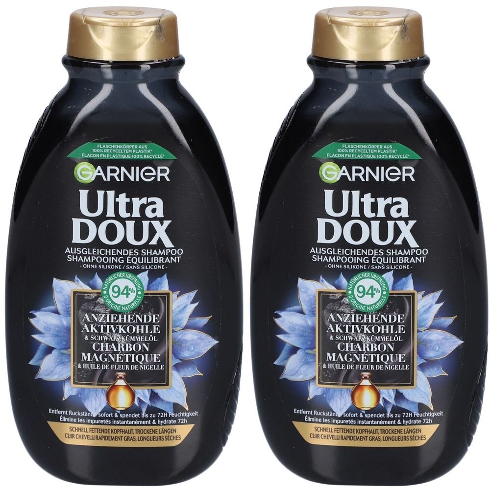 Twee zwarte shampoo flessen. Opschrift: GARNIER Ultra DOUX. Bevat actieve kool en zwarte komijnolie. Blauwe bloem en gouden dop.