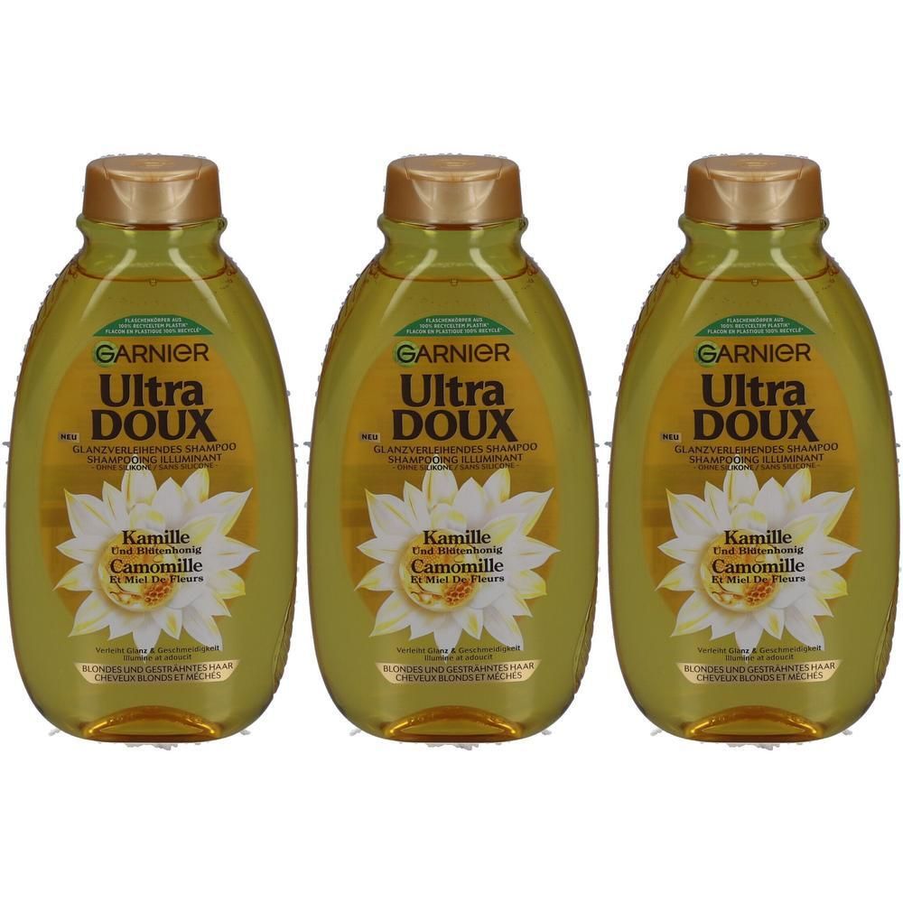 Drie flessen Garnier Ultra Doux Shampoo Illuminating Camomile. Gouden dop, gele vloeistof, kamillebloemlogo.