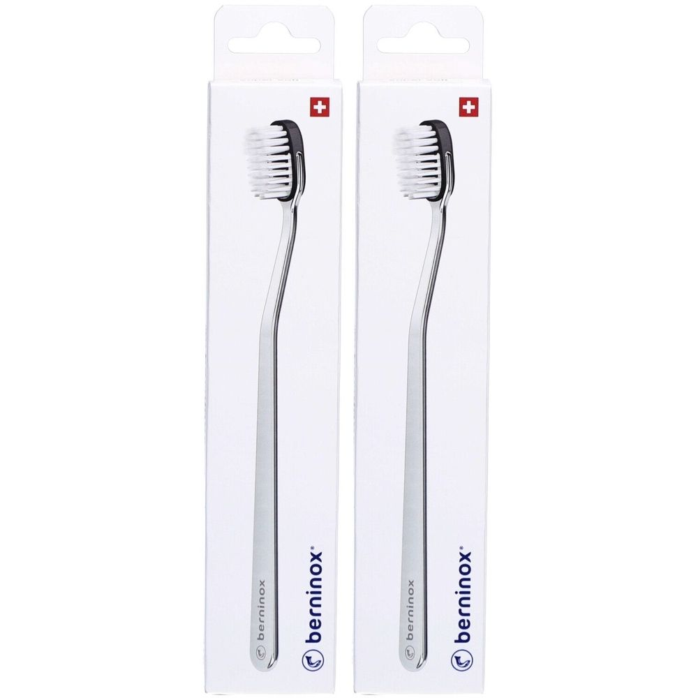 Deux brosses à dents dans des emballages blancs. Têtes de brosse noires, manches argentés. Croix suisse en haut à droite.