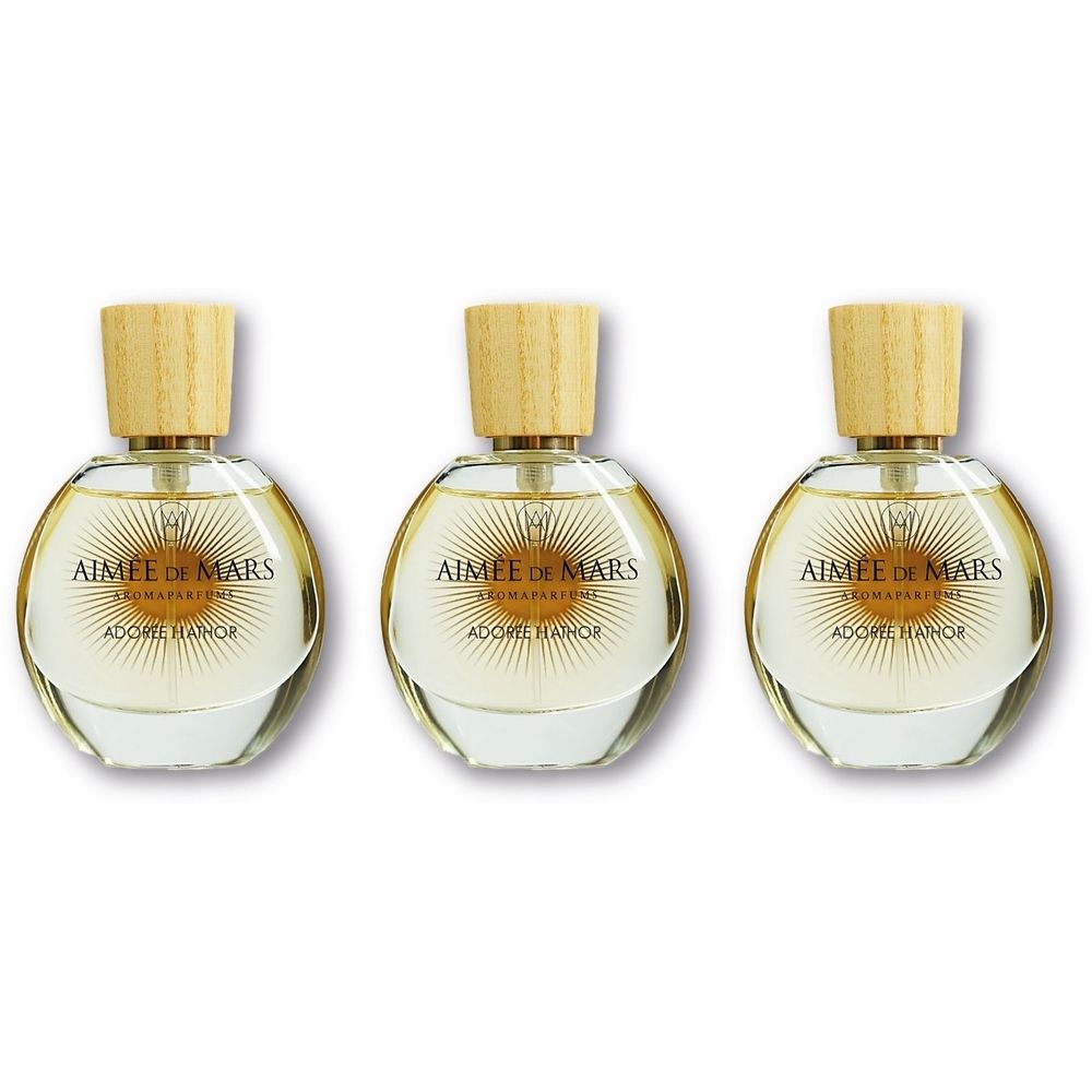 Drie ronde glazen flacons met houten dop. Opschrift: AIMEE DE MARS, ADORE HATHOR. Parfumflacons op witte achtergrond.