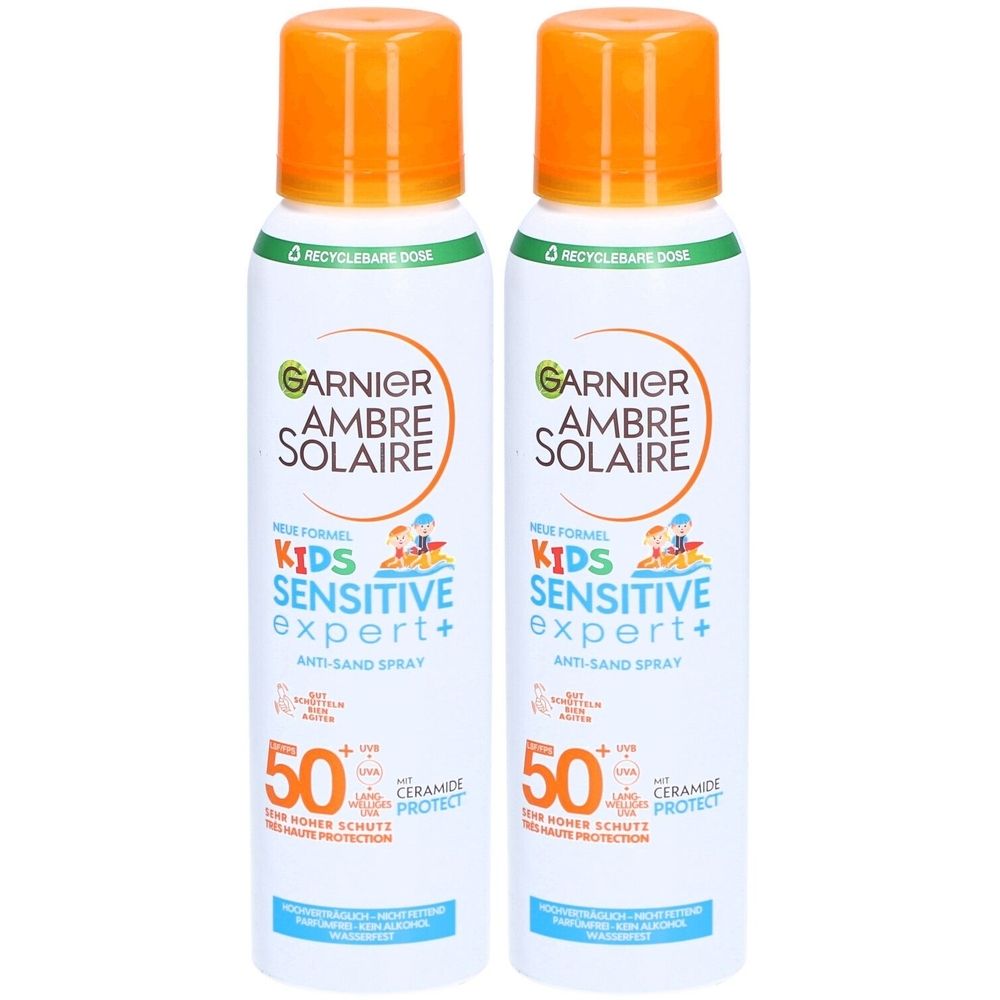 Twee sprays Garnier Ambre Solaire Kids Sensitive Expert+ SPF50+. Witte flessen met oranje doppen. Tekst: Anti-Sand Spray, 50, Ceramide Protect.