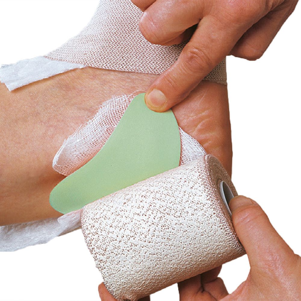 Application d'un bandage sur un pied. Un outil vert est utilisé pour façonner le bandage. Un rouleau de bandage est visible.