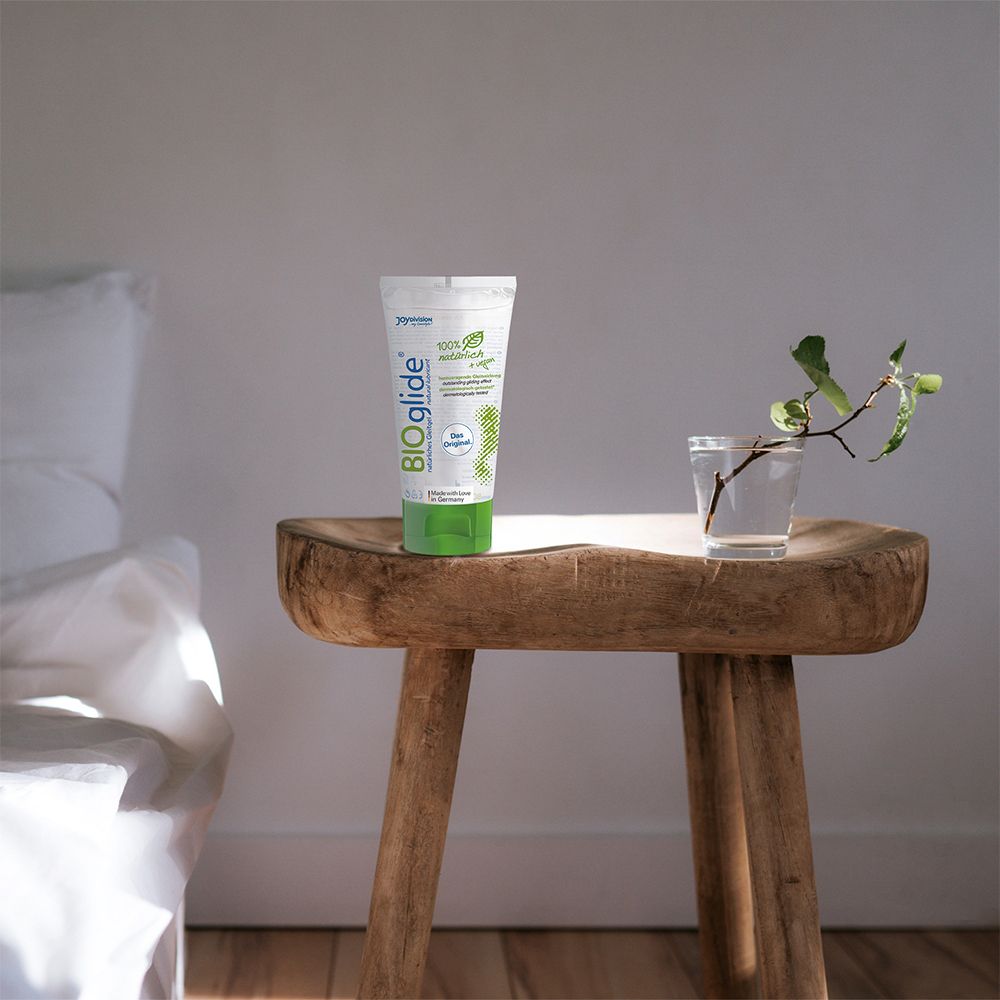 Tube BIOglide sur un tabouret en bois. À côté d'un verre d'eau et d'une branche. Chambre blanche.