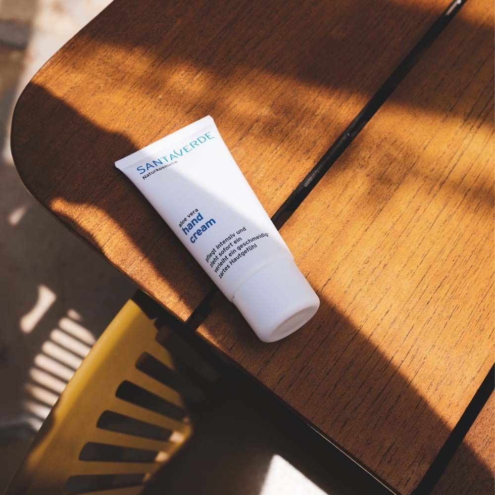Tube blanc de crème pour les mains SANTAVERDE sur une surface en bois. Nom du produit et texte : hand cream. Partiellement à l'ombre.