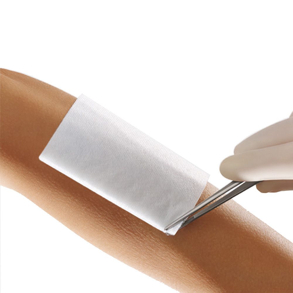 Compresse blanche sur bras. Ciseaux coupent la compresse. Gants stériles.